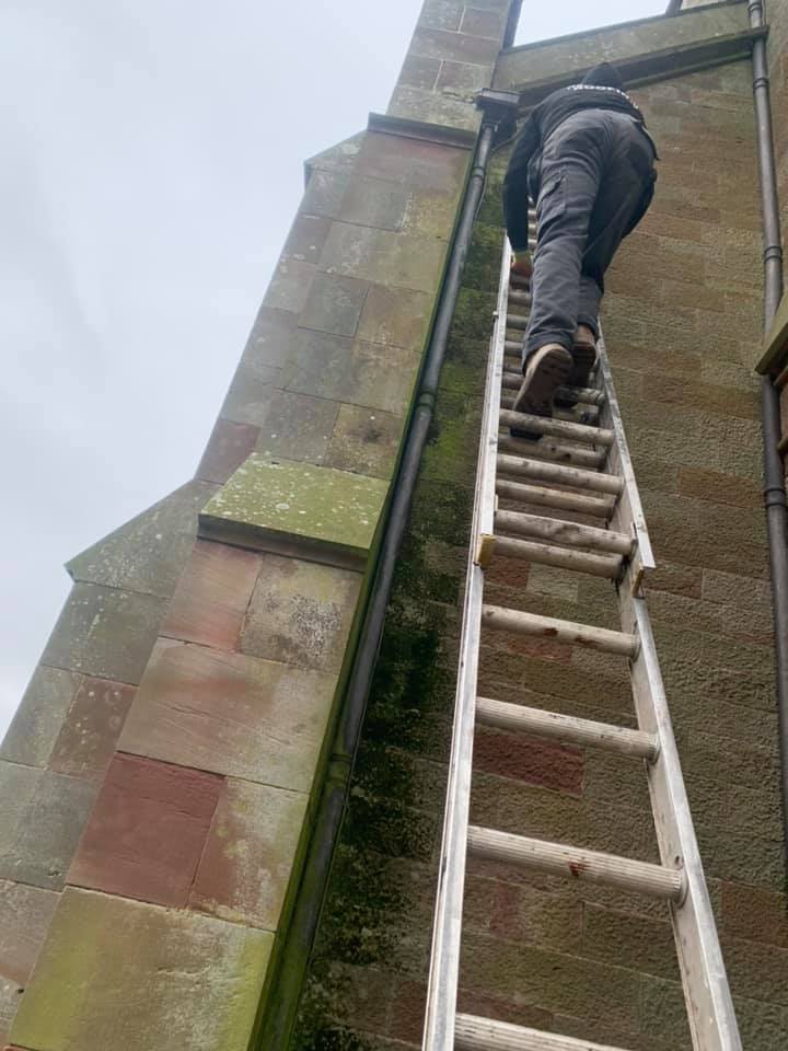 Roofer climbing up a ladder on a church